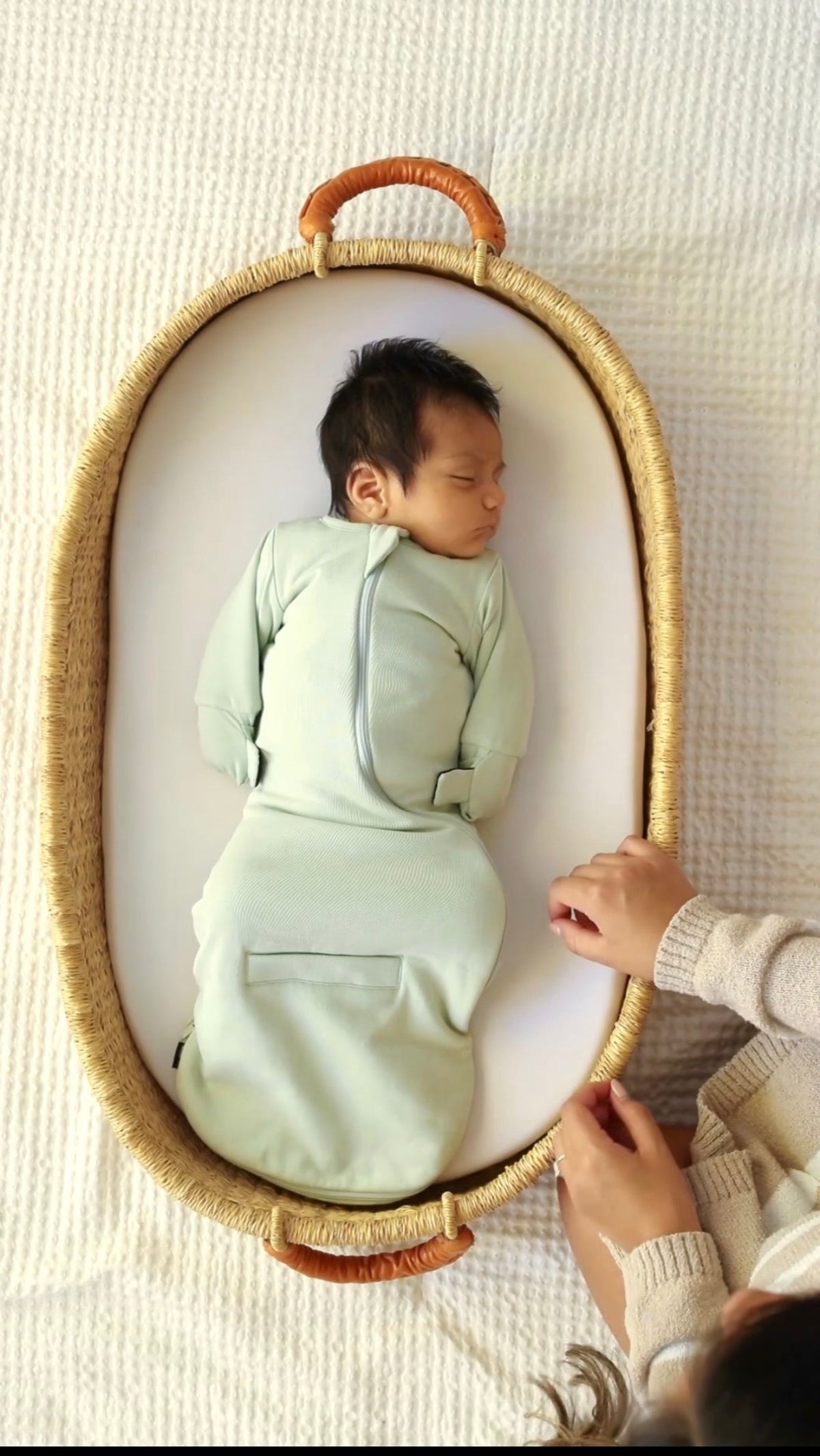 Baby asleep on their back in a basket in a Sage Green Swaddle Easy, mittens folded over and down by the sides