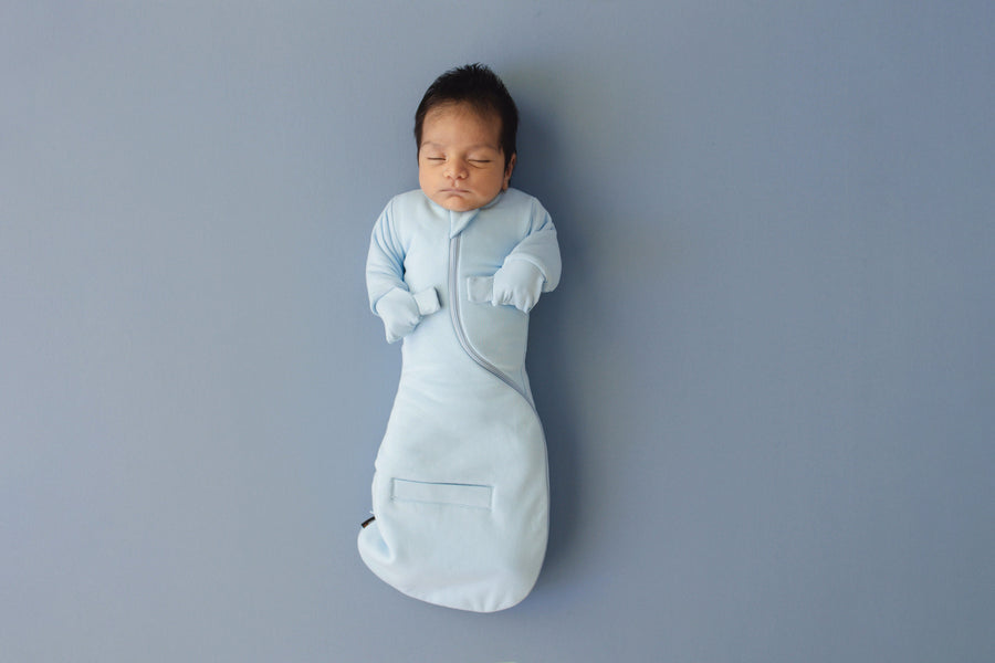 Newborn asleep on their back in a Sky Blue Swaddle Easy, mittens folded over on the chest