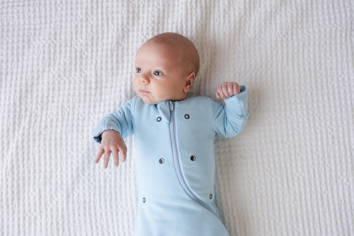 Awake baby on their back in a Sky Blue Swaddle Easy with both hands out