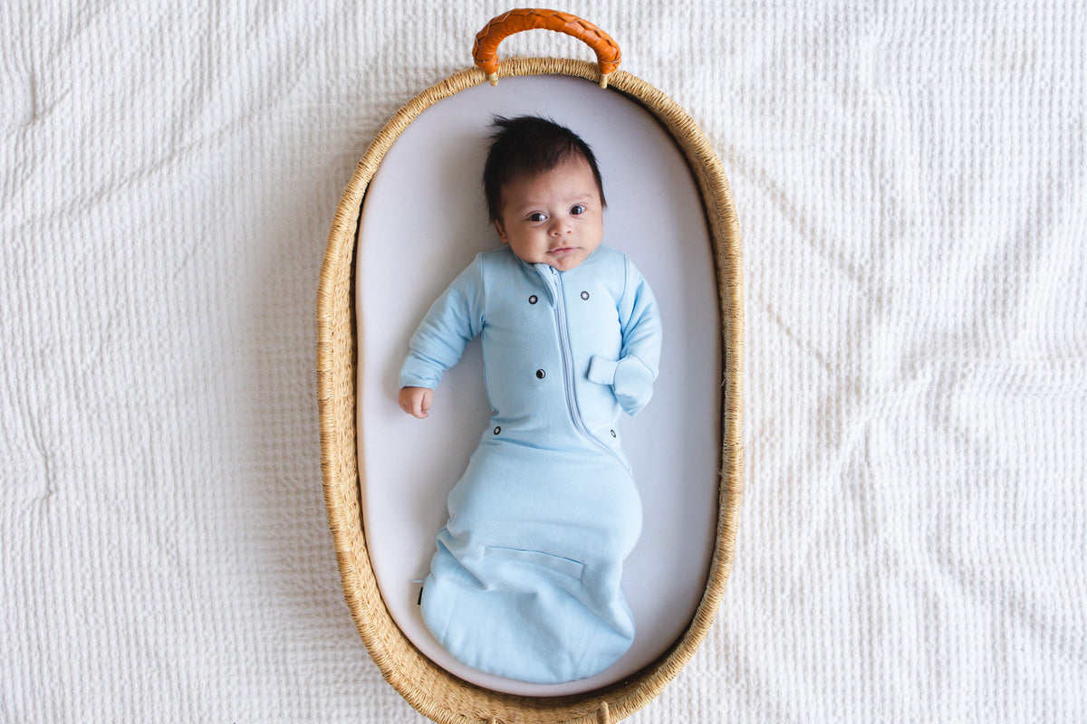 Awake baby on their back in a woven basket in a Sky Blue Swaddle Easy