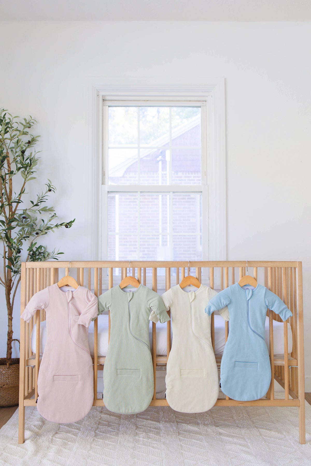 Swaddle Easy in Light Pink, Sage Green, Cream and Sky Blue hanging on a wooden crib in a bright nursery