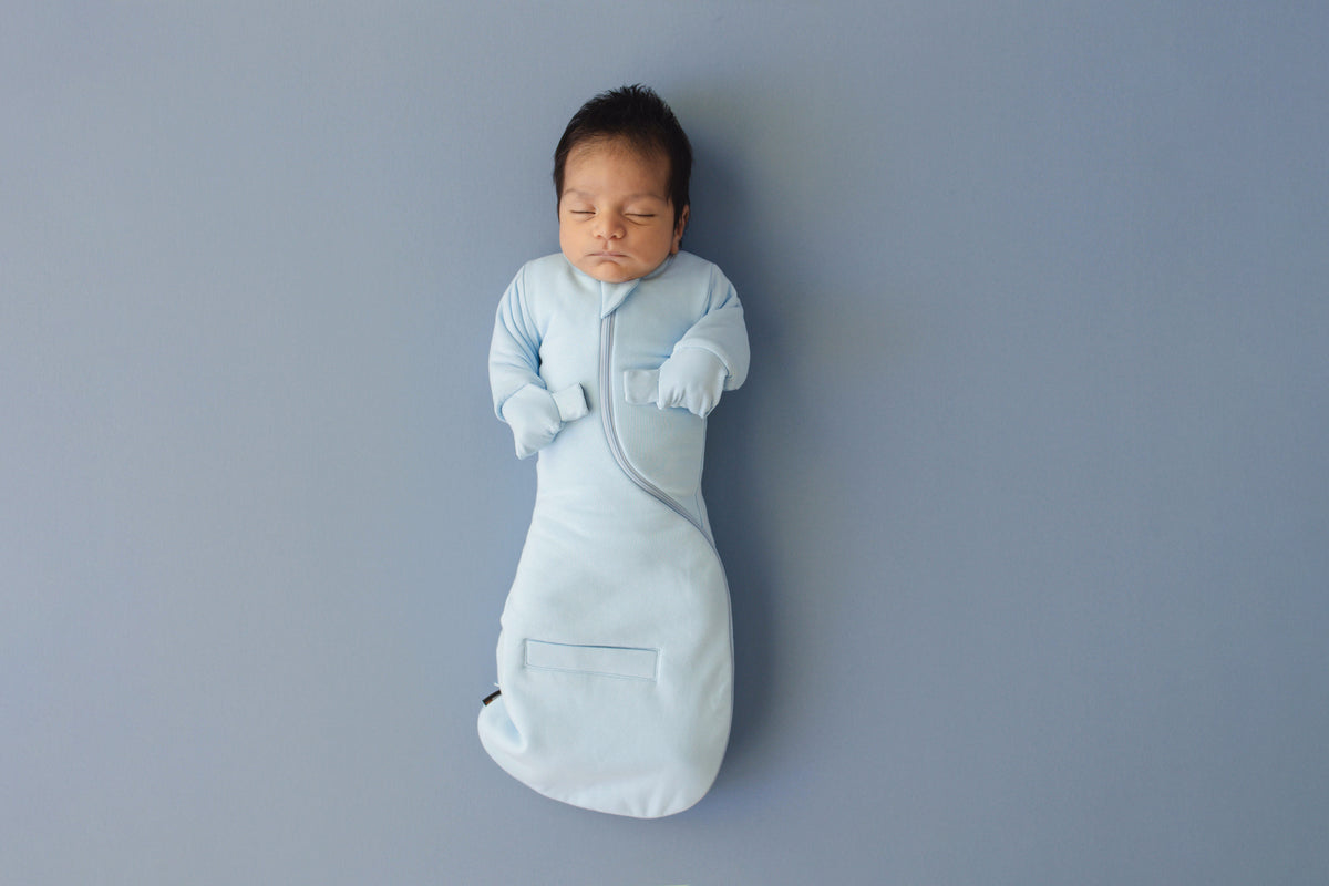 Newborn asleep on their back in a Sky Blue Swaddle Easy, mittens folded over on the chest