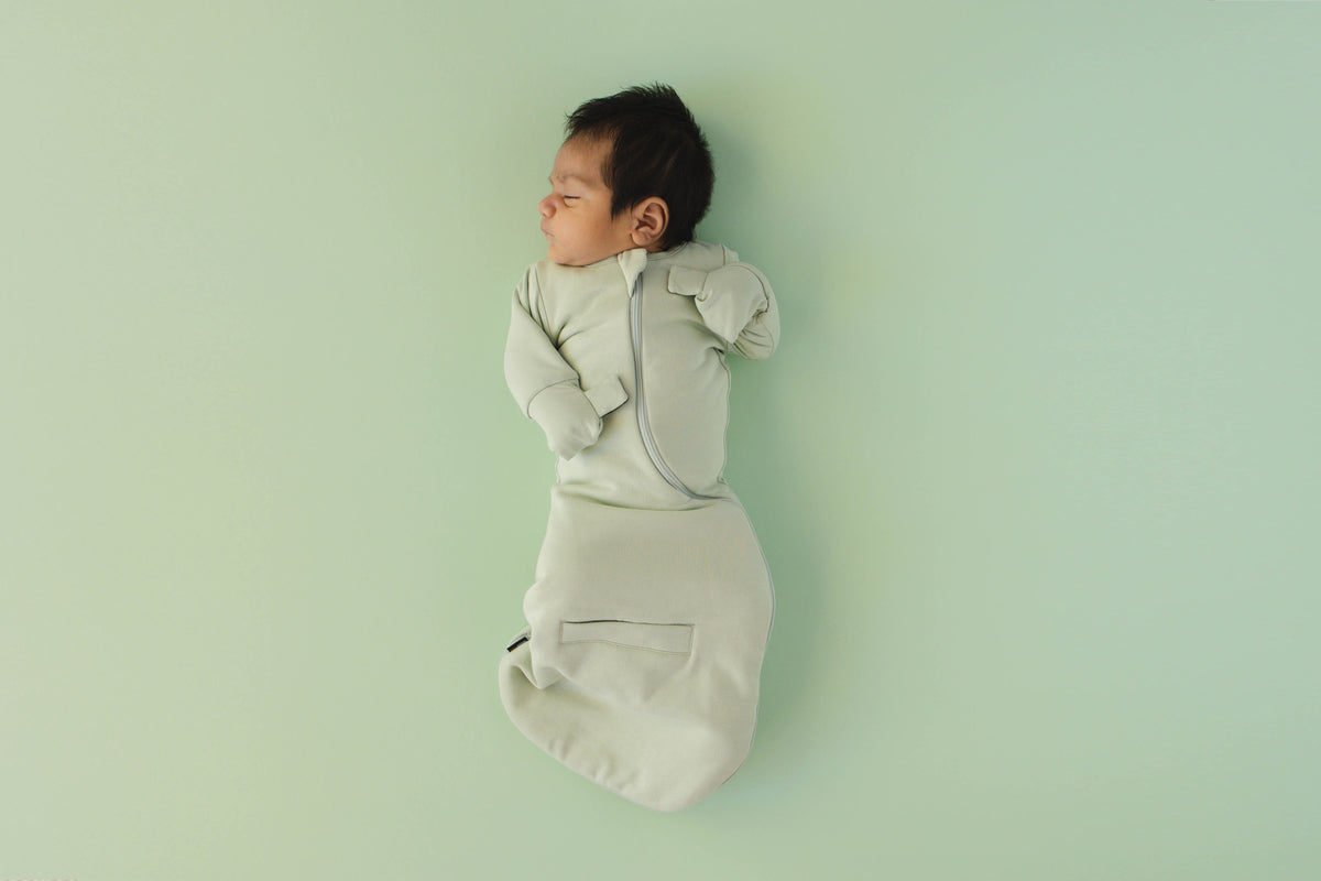 Newborn asleep on their back in a Sage Green Swaddle Easy, mittens folded over with hands up