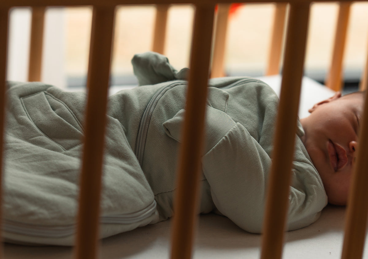 Newborn asleep on their back in a Sage Green Swaddle Easy in a wooden crib