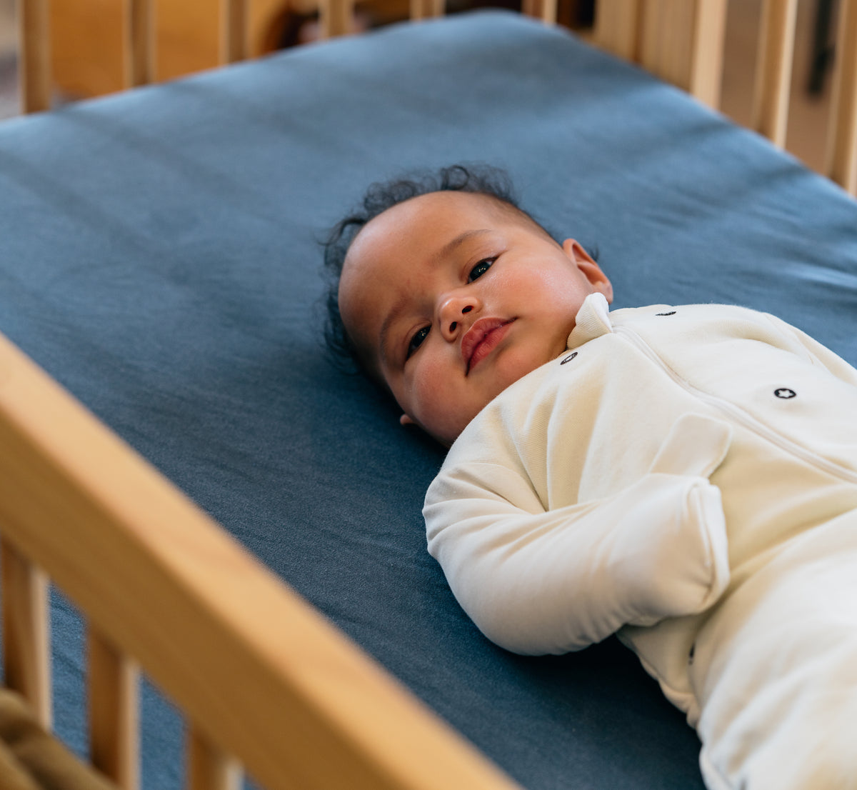 Awake baby on their back in a Cream Swaddle Easy in a crib with a blue sheet