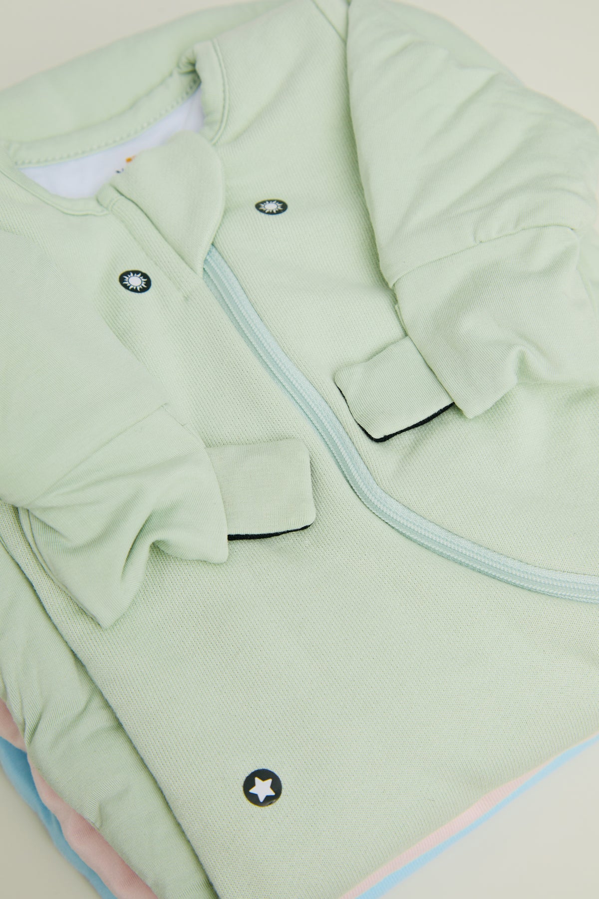 Close-up of a Sage Green Swaddle Easy showing the covered magnet dots, a folded mitten with its tab and the zipper