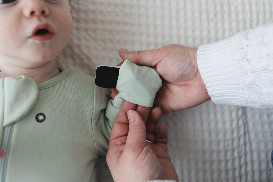 A parent folds the magnetic mitten closed on a Sage Green Swaddle Easy