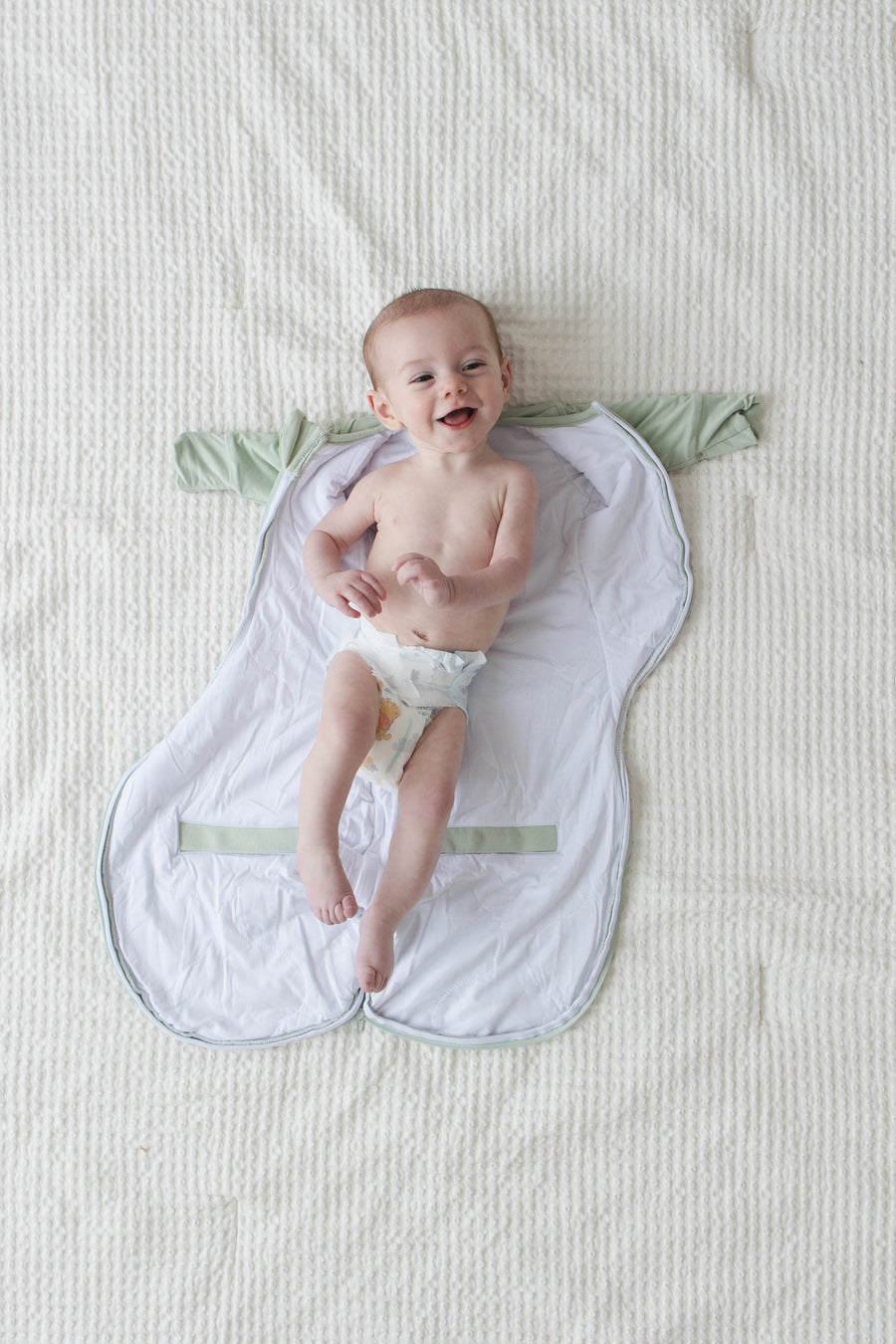 Smiling baby lying on an open Sage Green Swaddle Easy before it is zipped