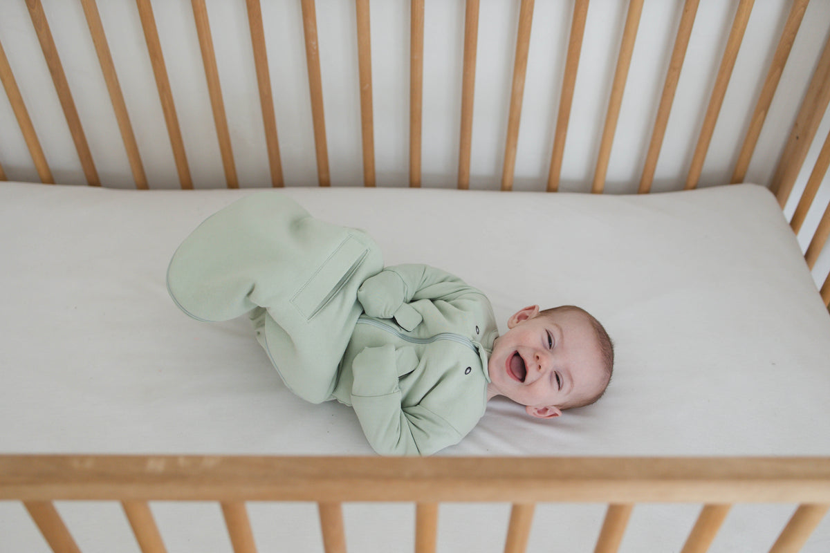 Smiling awake baby in a Sage Green Swaddle Easy lying on their back in a crib