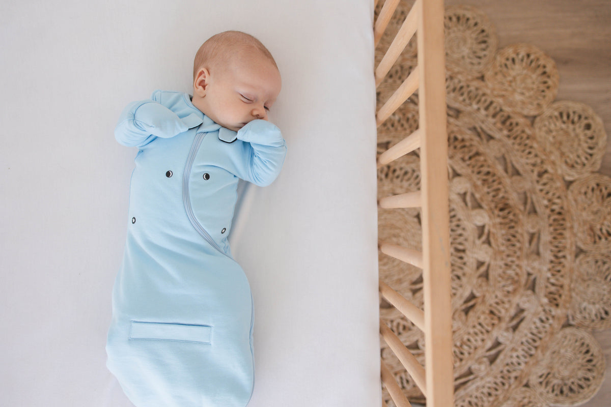 Baby asleep on their back in a Sky Blue Swaddle Easy, mittens folded over with hands up near the face