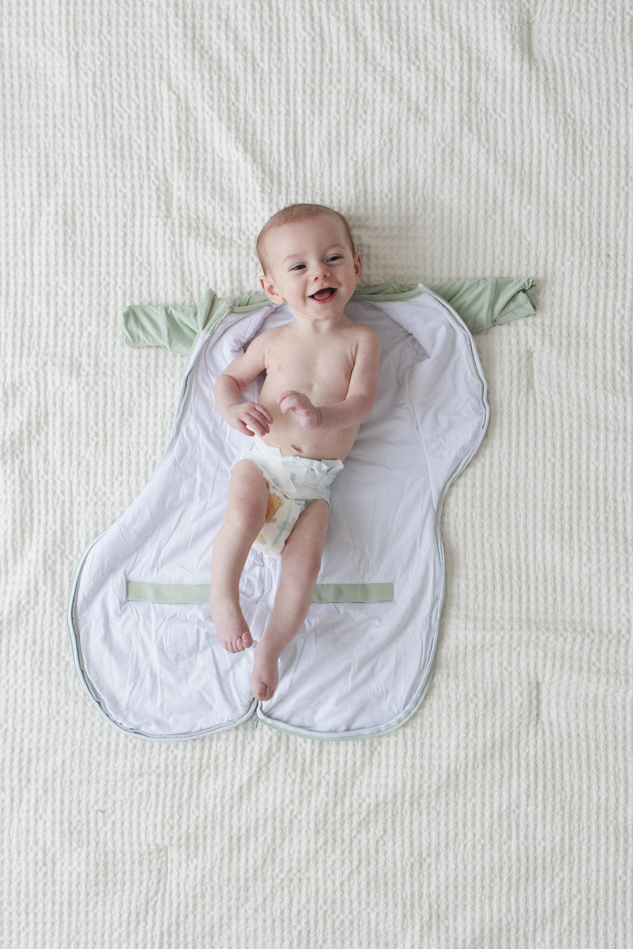Smiling baby lying on an open Sage Green Swaddle Easy before it is zipped
