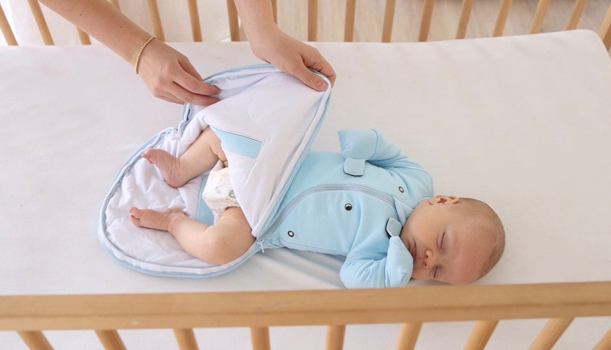 A parent opens the bottom zipper of a Sky Blue Swaddle Easy for a diaper change in a crib