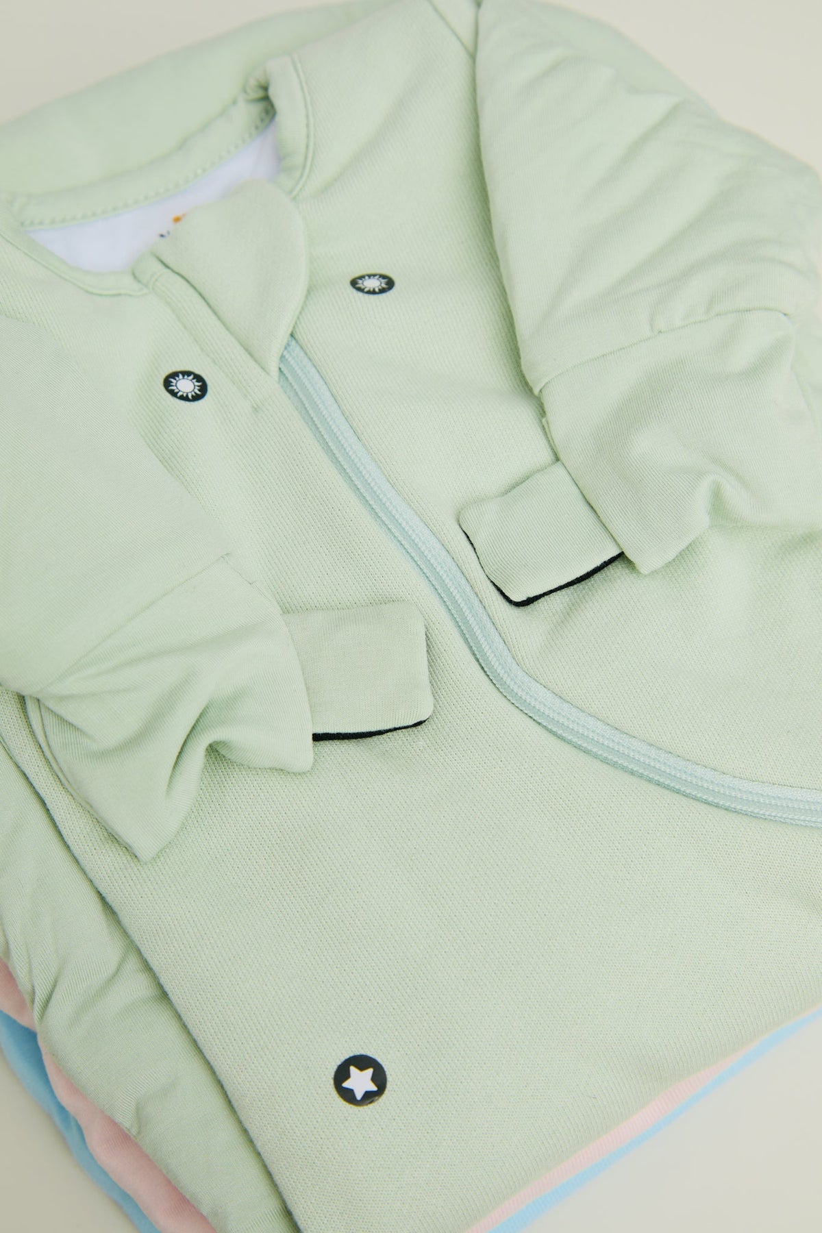 Close-up of a Sage Green Swaddle Easy showing the covered magnet dots, a folded mitten with its tab and the zipper