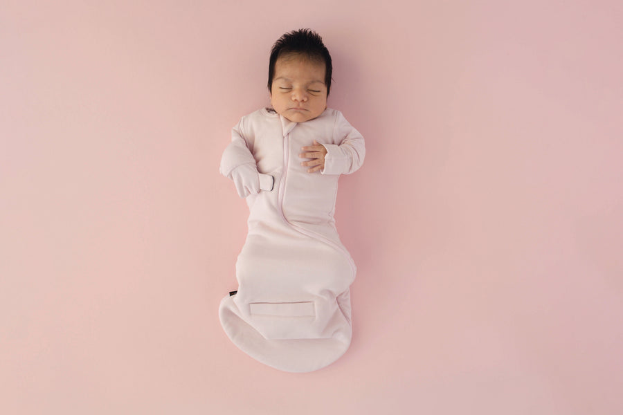 Newborn asleep on their back in a Light Pink Swaddle Easy, mittens folded over with hands up