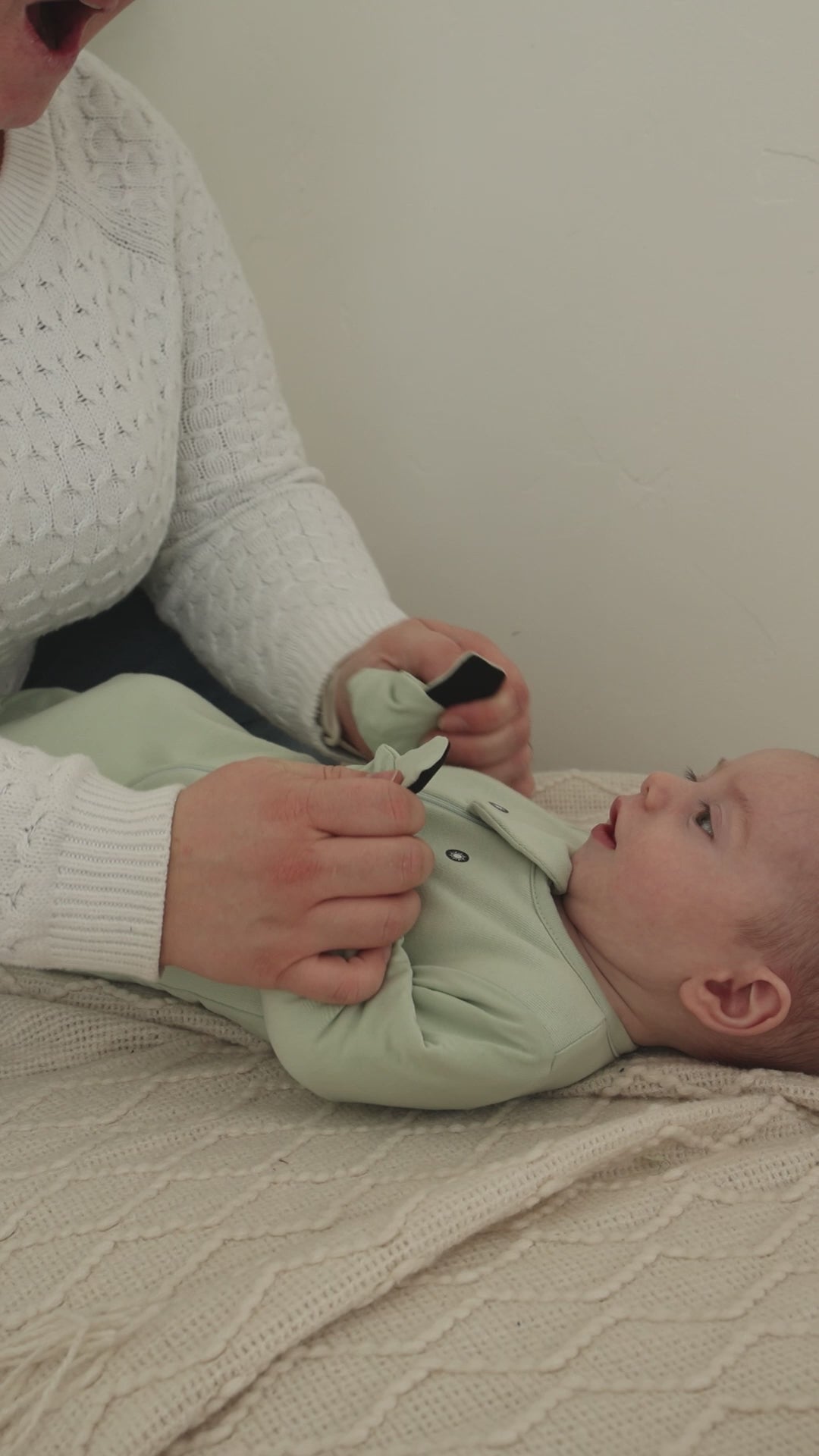 A mom folds the magnetic mittens over on a Sage Green Swaddle Easy and they click shut