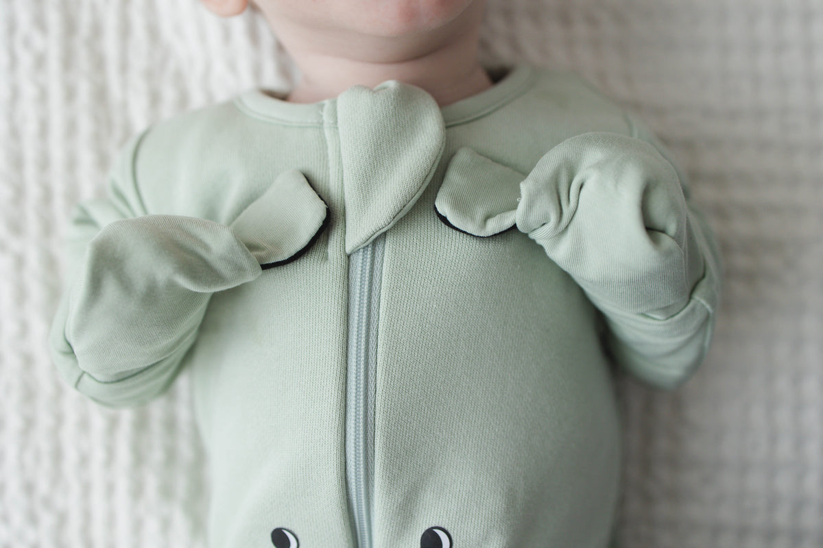 Close-up of Sage Green mittens folded over on a baby’s chest