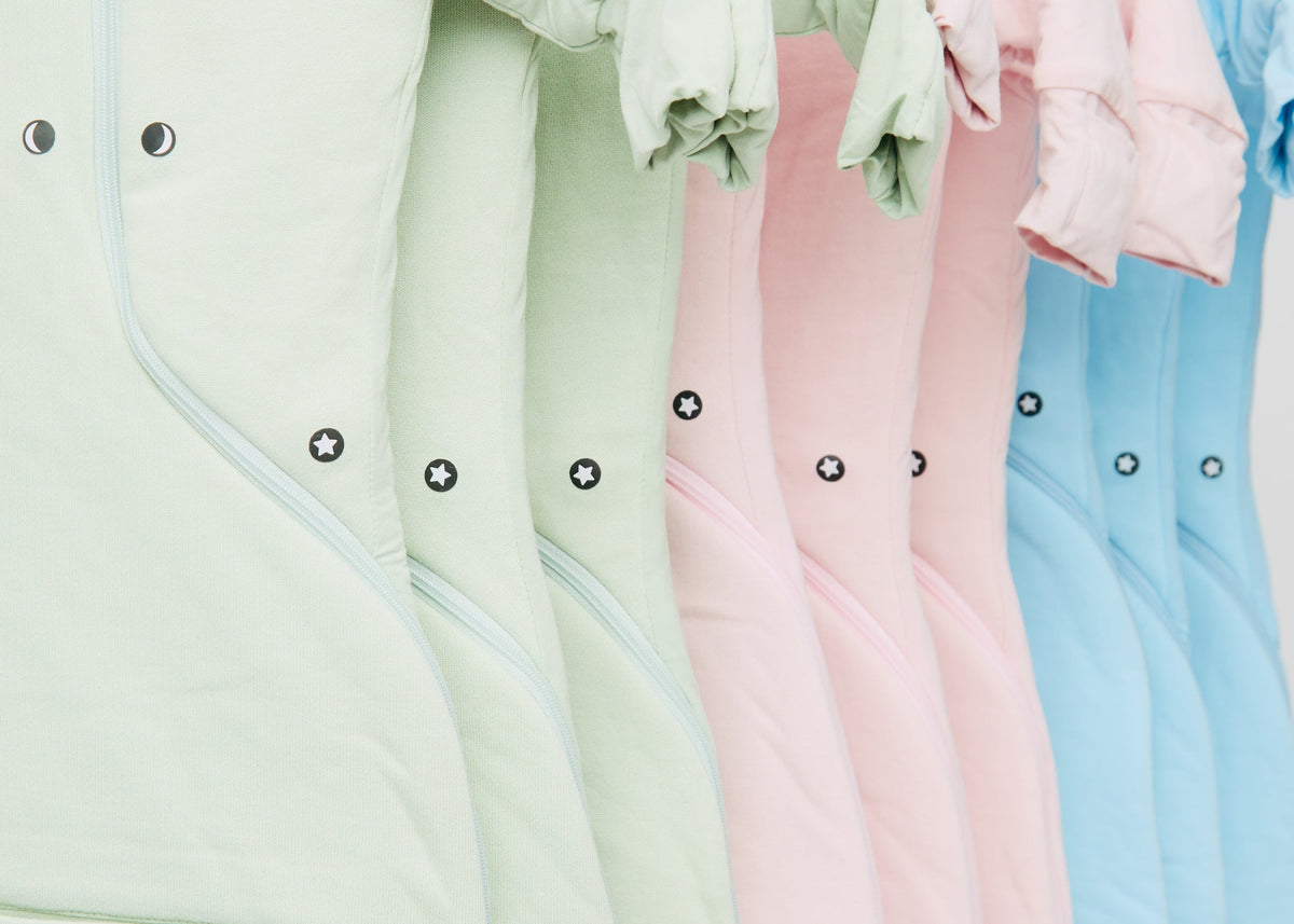 Sage Green, Light Pink and Sky Blue Swaddle Easy sacks hanging in a row, showing the magnets